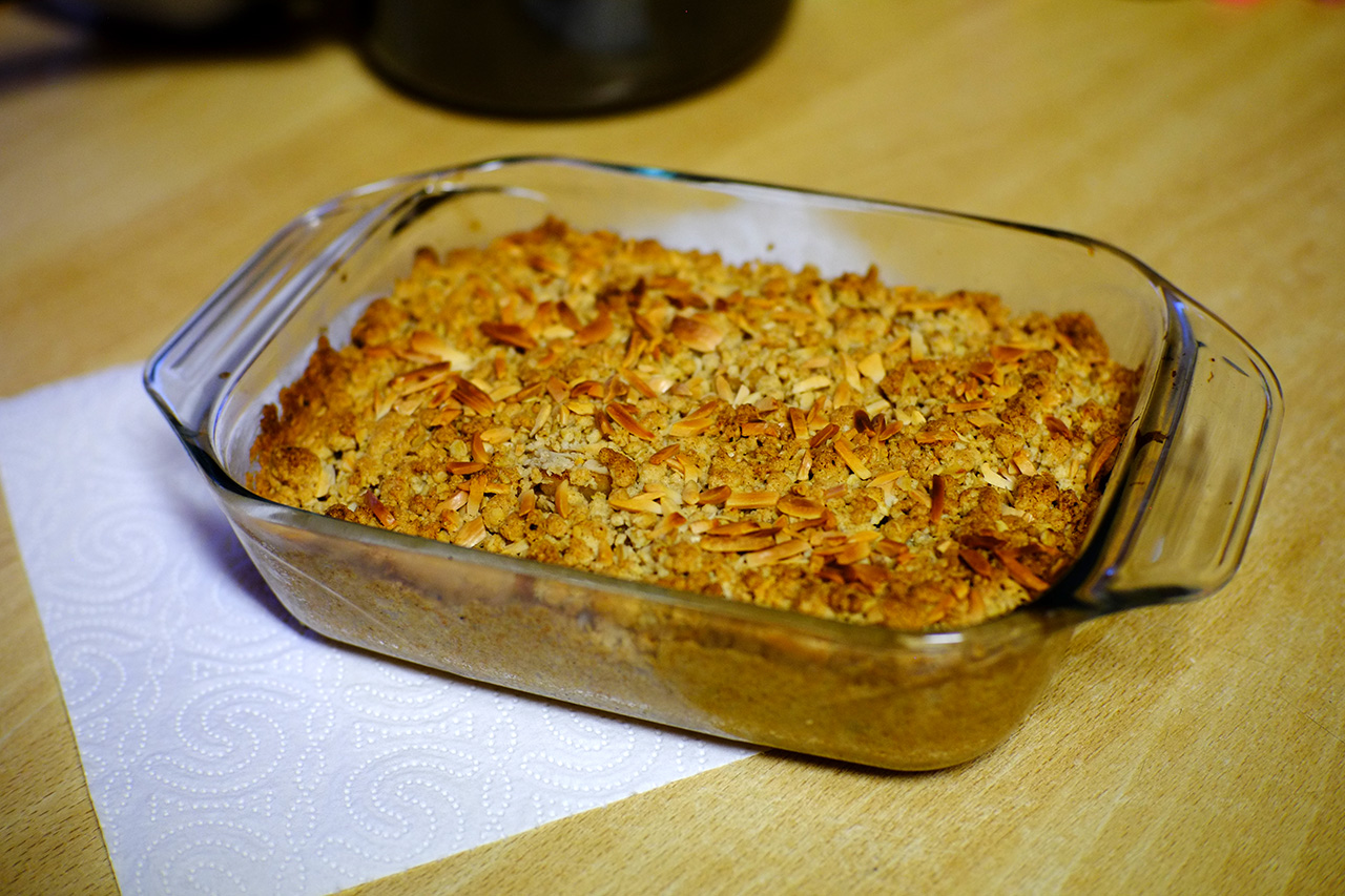 A photo of an apple crumble pie in a glass baking dish on top of a wooden table.