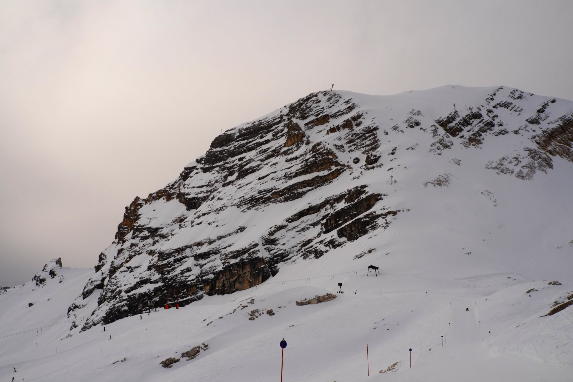 A photo of a brown rocky mountain cliff covered partly with snow.