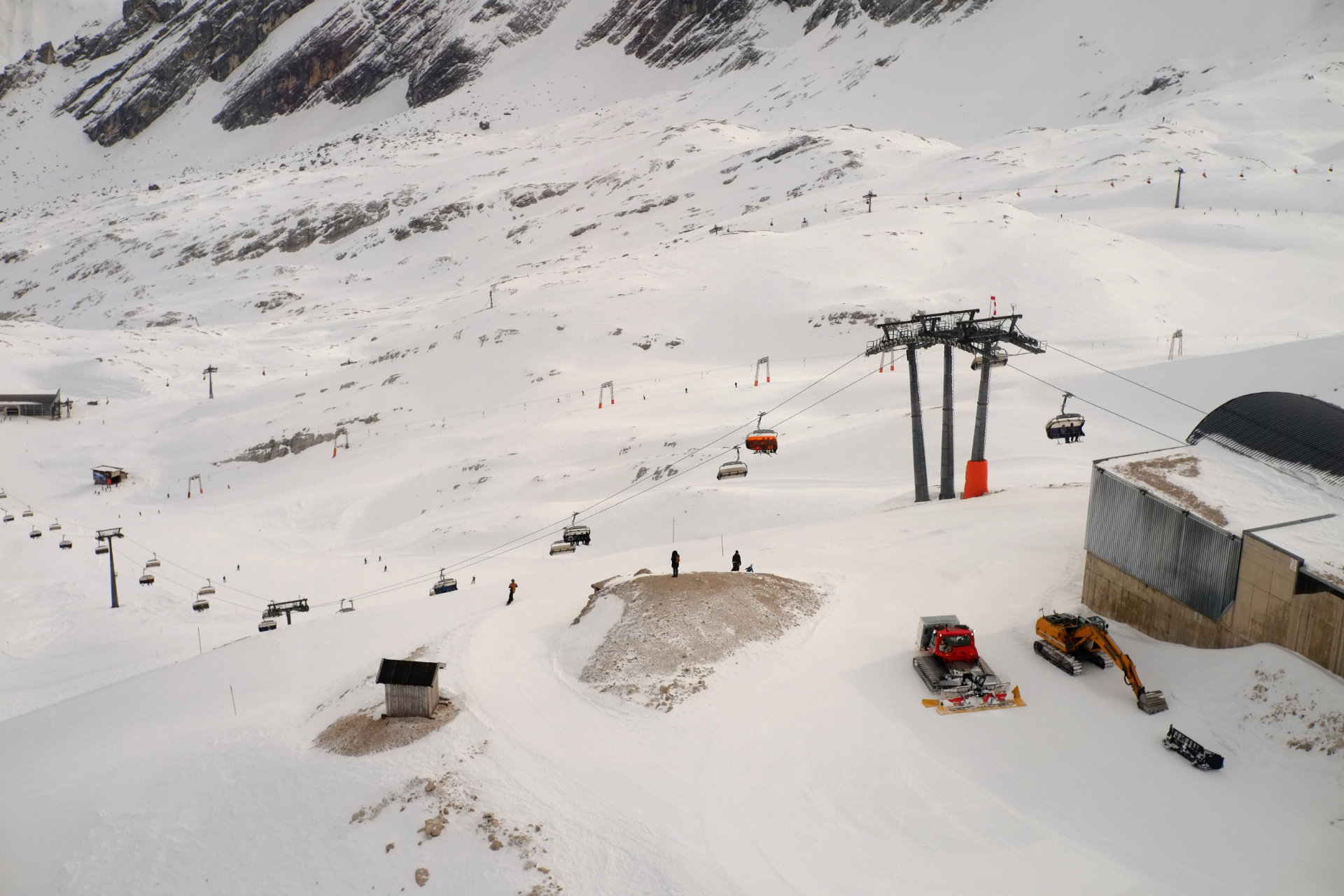 A photo of the various skiing slopes from above with several ropeways going along the slopes and some maintenance vehicles parked on top of the closest slope.
