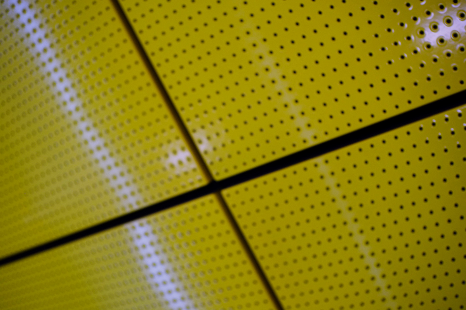 A blurry close-up photo of glossy yellow ceiling tiles with rows of holes in them.