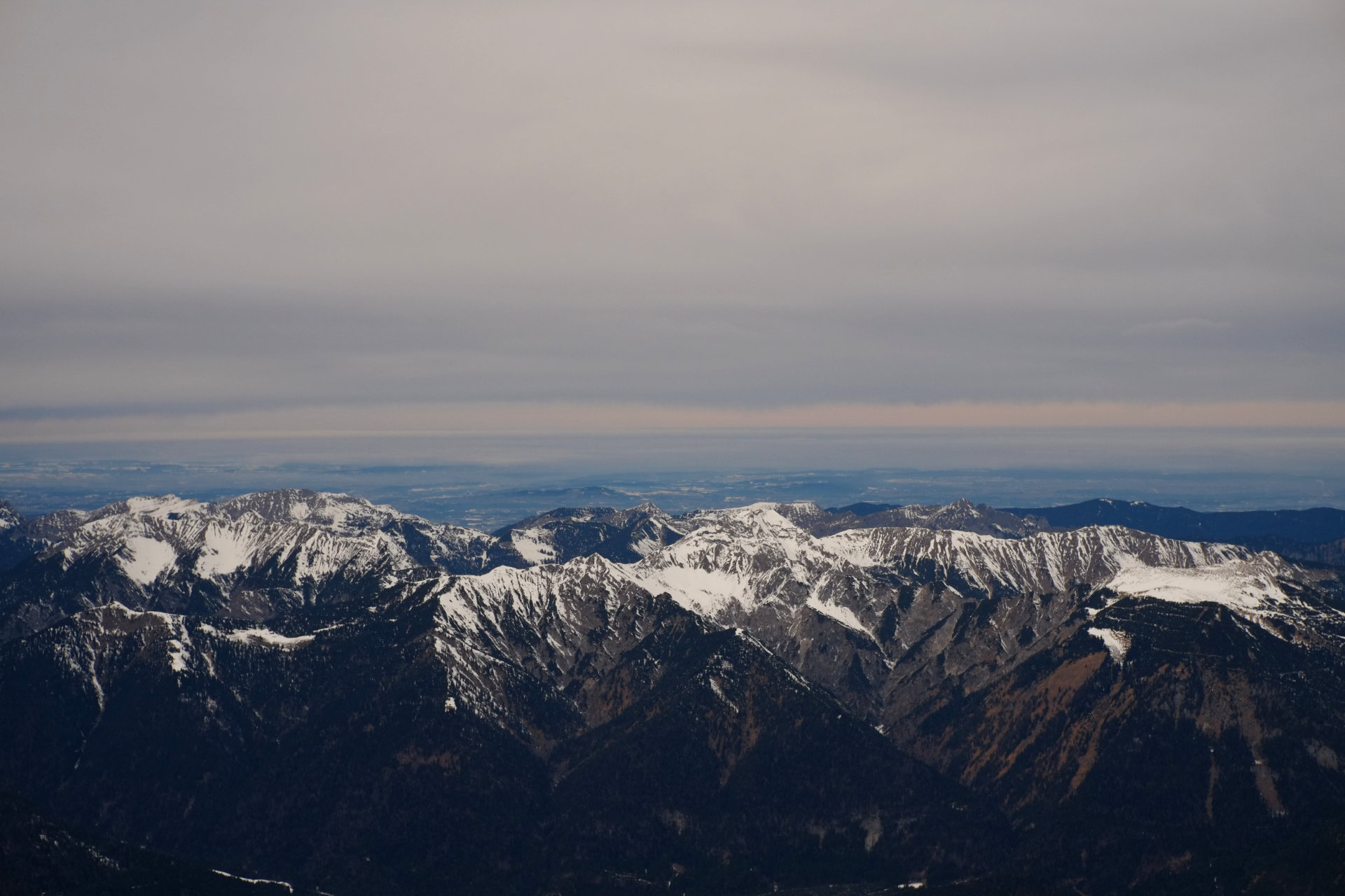 A photo of dark mountains from above and plains behind them disappearing into the horizon.