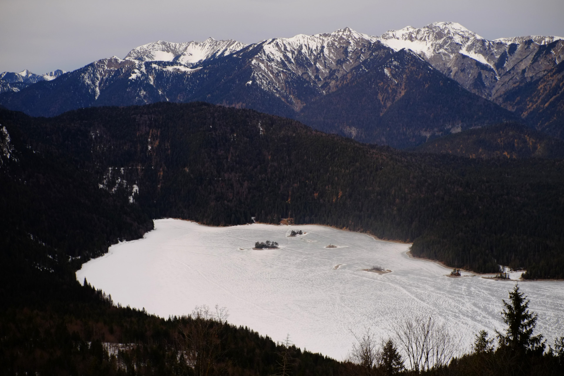 A photo of a big lake among snowy mountains and pine forests, completely covered with snow and ice, shot from a big height.