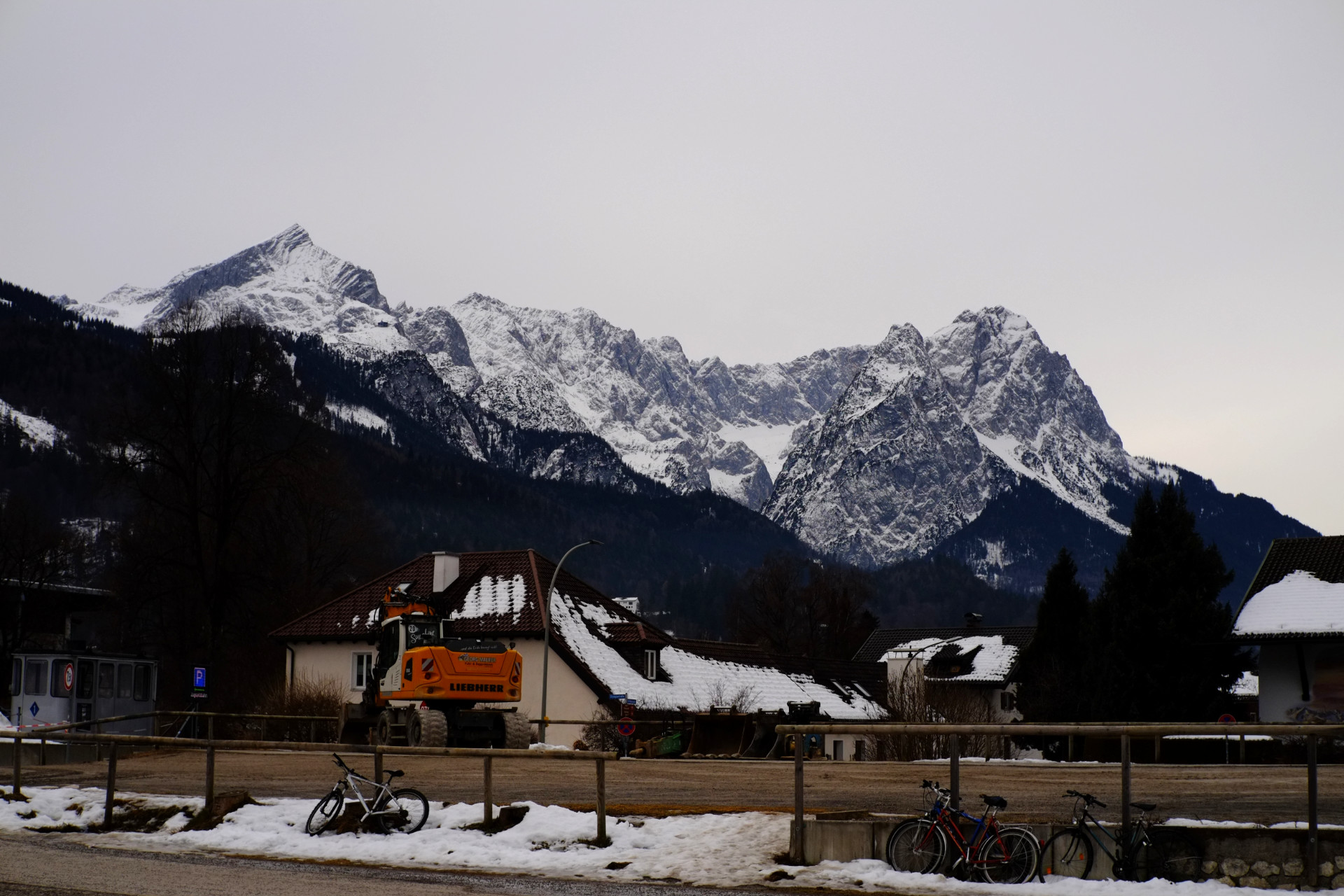 A photo of a train station platform with low town buildings behind it, an orange excavator, and a high snowy mountain in the background.
