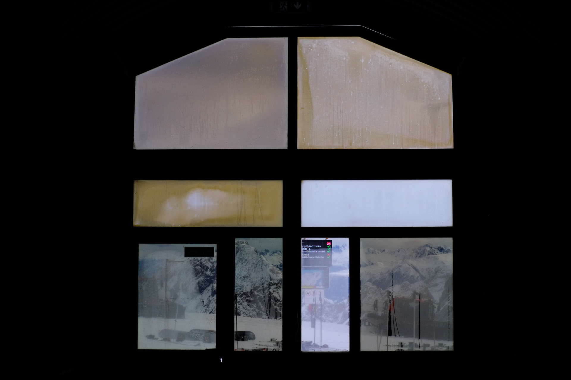 A photo of the tunnel station window all parts of which have different hues (yellow, gray, blue) with snowy peaks of the Alps visible through it.