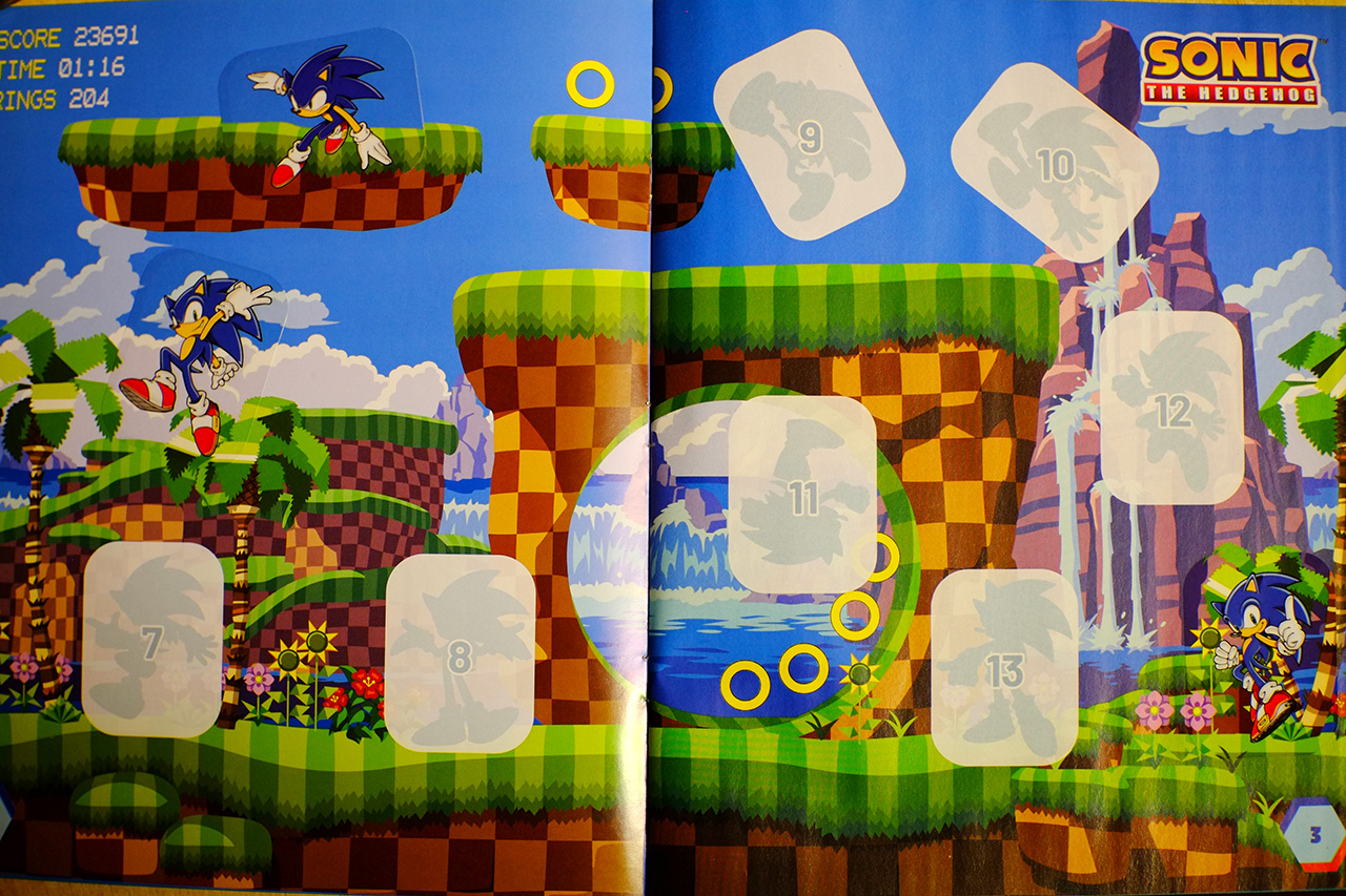 A photo of a page spread from Sonic the Hedgehog sticker album, featuring the Green Hill Zone background and three stickers with Sonic running and jumping around.