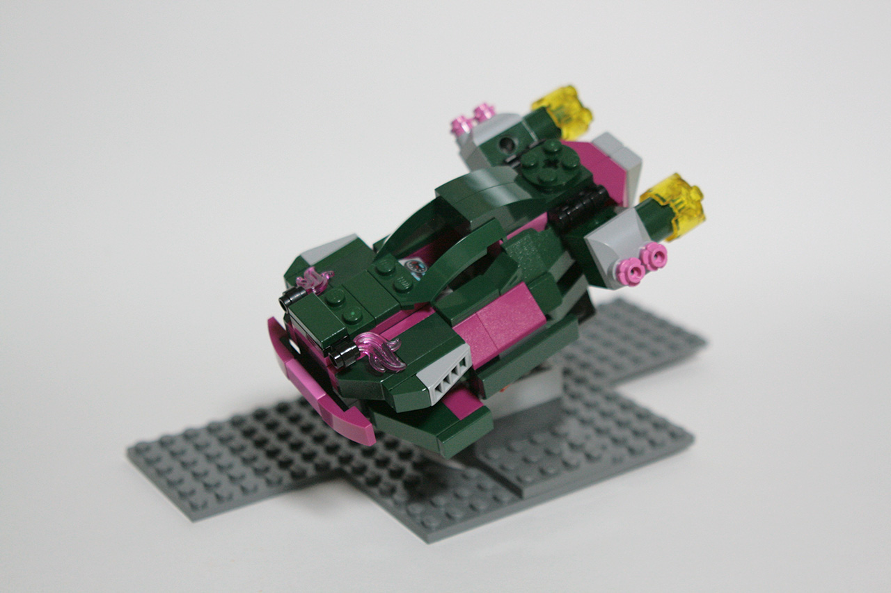 A photo of my improvised lego hovercar build. It's a dark green futuristic flying car with magenta elements and a few light grey details. There are two futuristic engines on the sides in the back of the car. The build itself is hovering above ground for the photo, supported by a structure built out of grey lego pieces and a big grey lego platform.