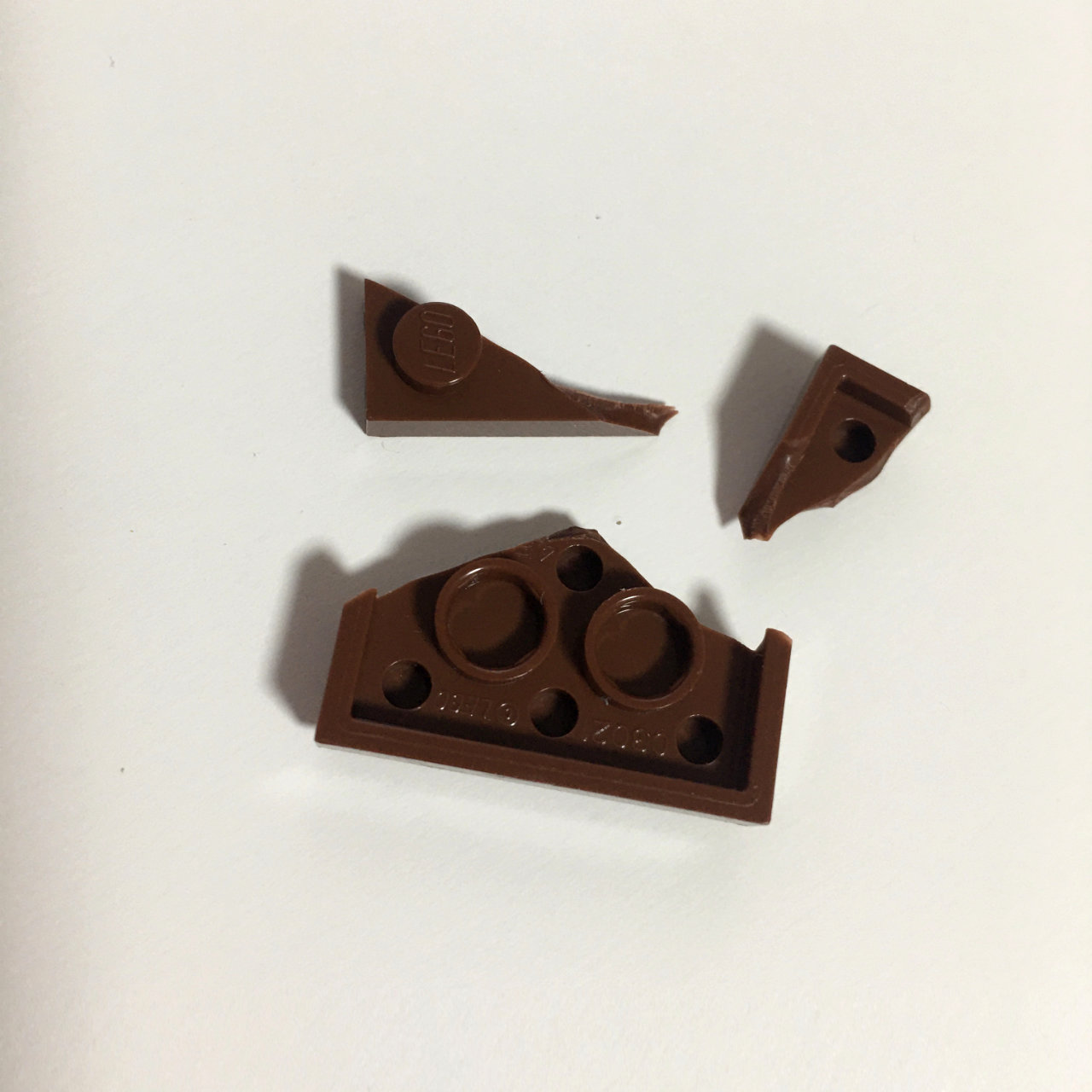 A photo of a broken into three pieces LEGO 2 by 2 platform piece.