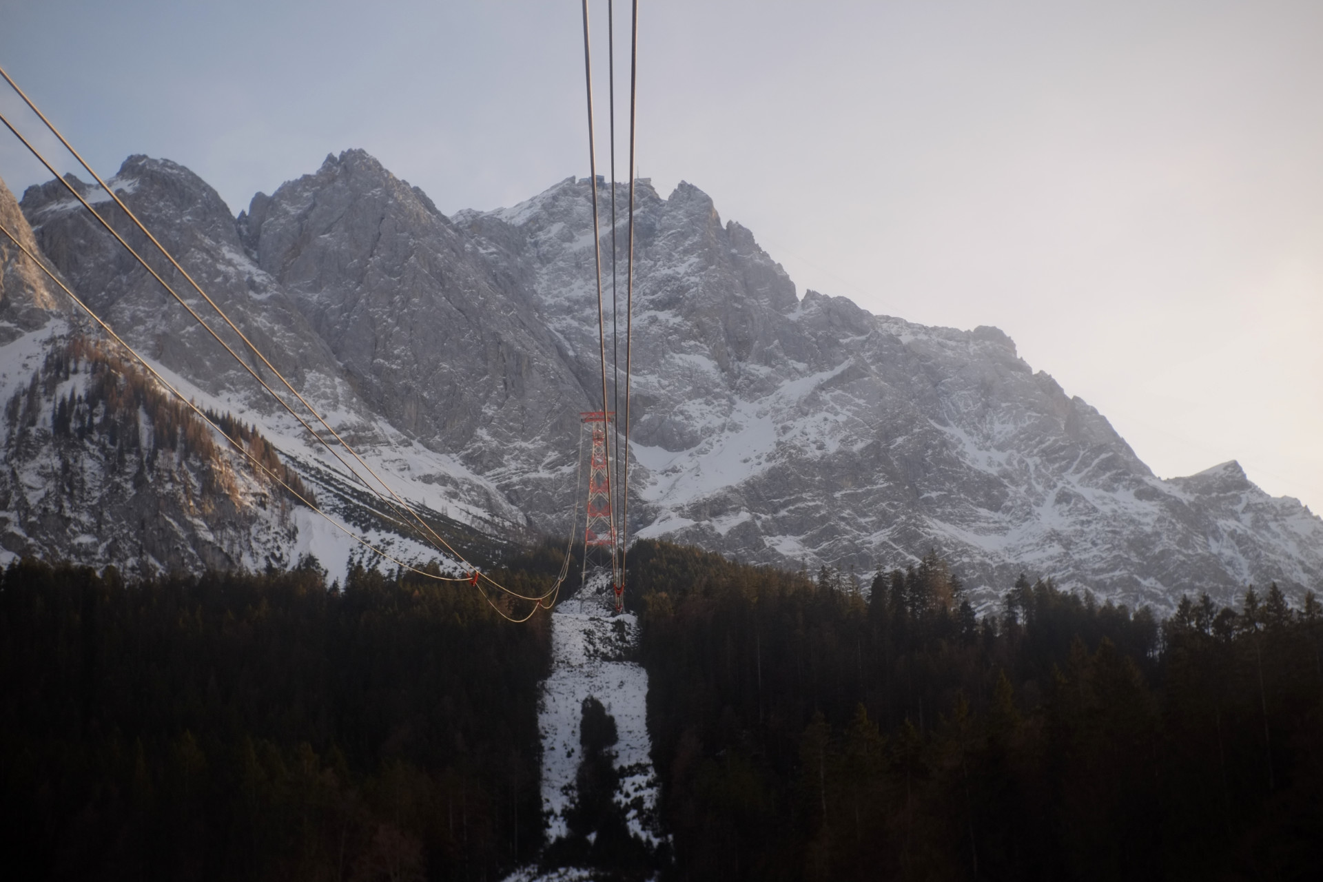 A photo of cable car cables going up the mountain to the peak station supported by red and white steel towers.