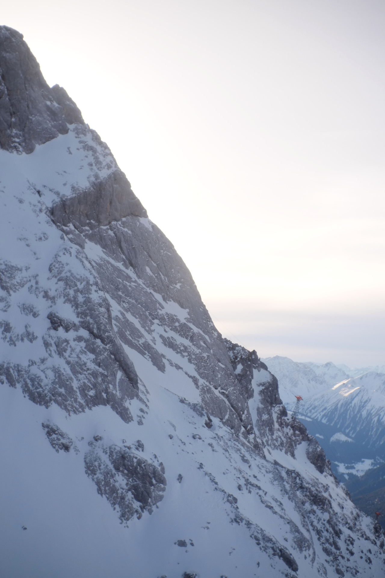 A photo of the snowy mountain cliff and bright white sky behind it.