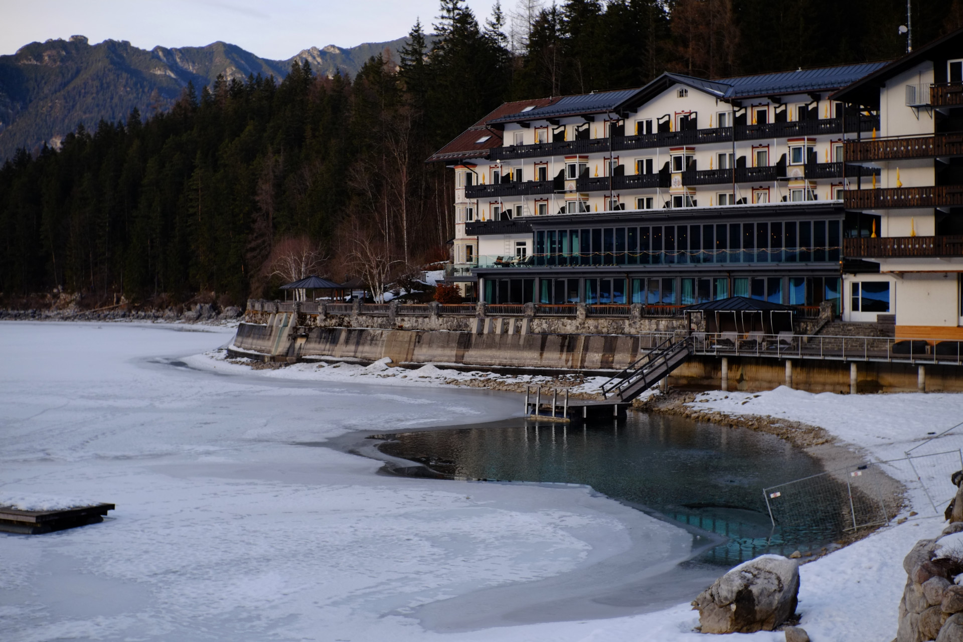 A photo of a hotel building right at the lake shore. The lake surface is partly frozen.