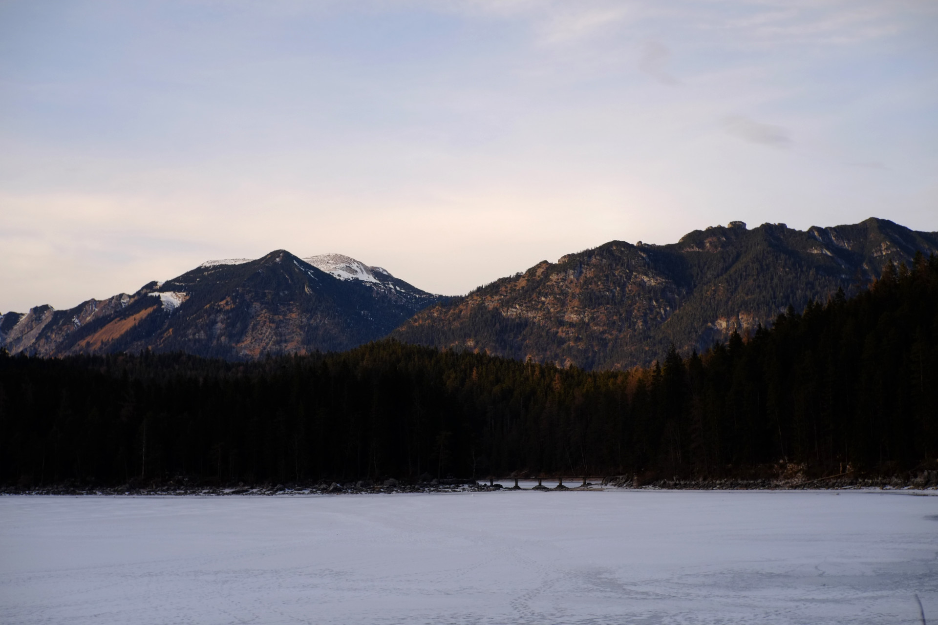 A photo of a frozen lake with dark mountains lit by the evening sun behind it.