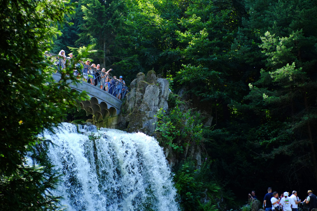 A photo of a waterfall and a metal bridge above it with several tourist on it looking down.