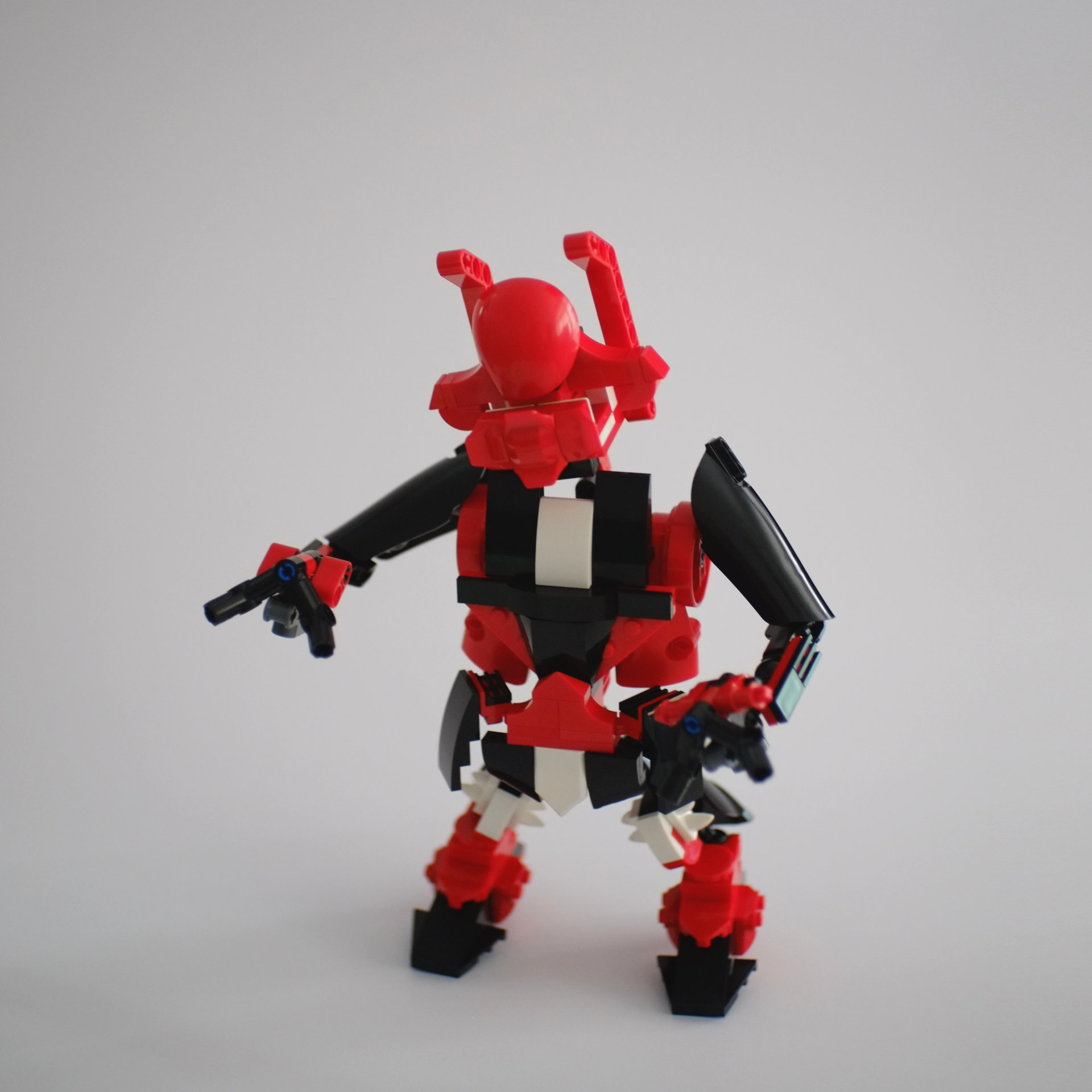 A photo of a lego build featuring a humanoid looking robot in red, black, and white with one arm pointing at something. Shot from the front.