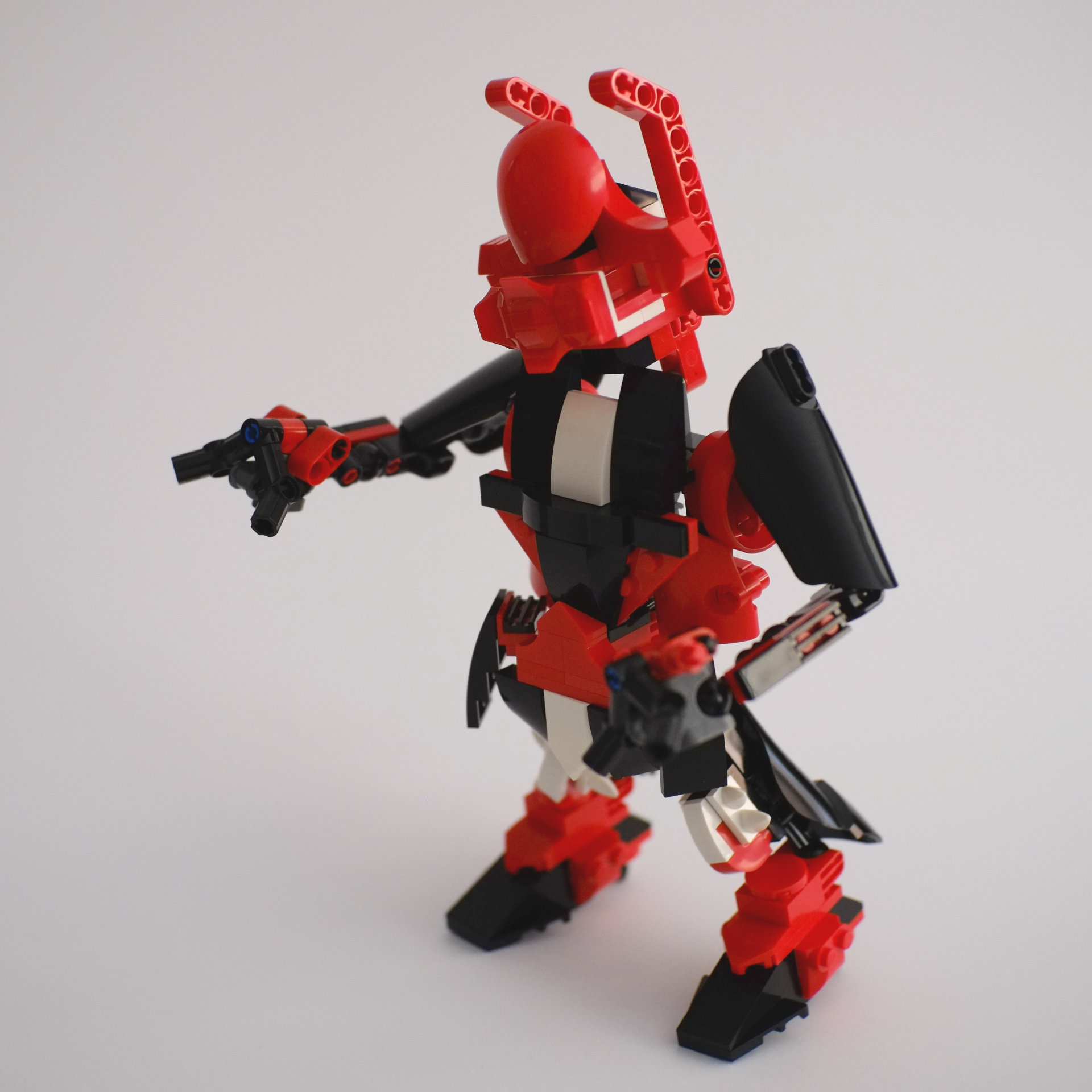 A photo of a lego build featuring a humanoid looking robot in red, black, and white with one arm pointing at something.