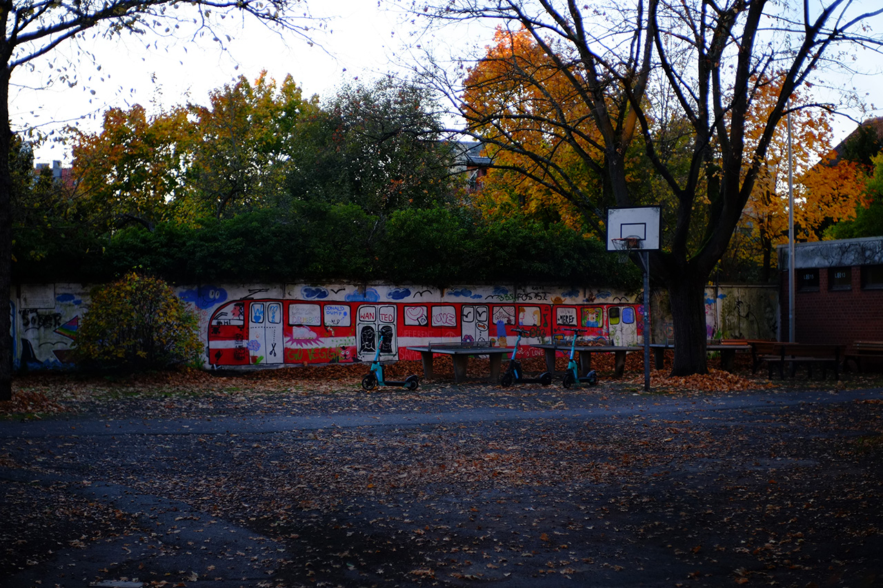 A photo of a playground with a concrete wall in the background and a red tram painted on it.