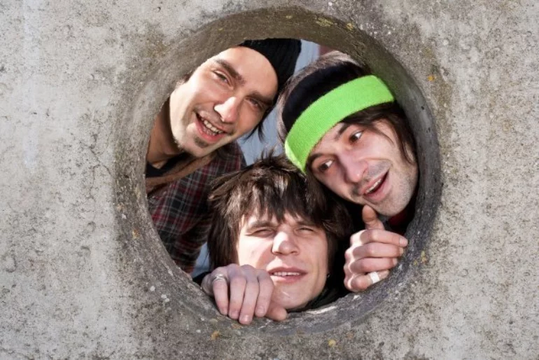 A photo of three smiling men looking through a hole in a concrete wall.