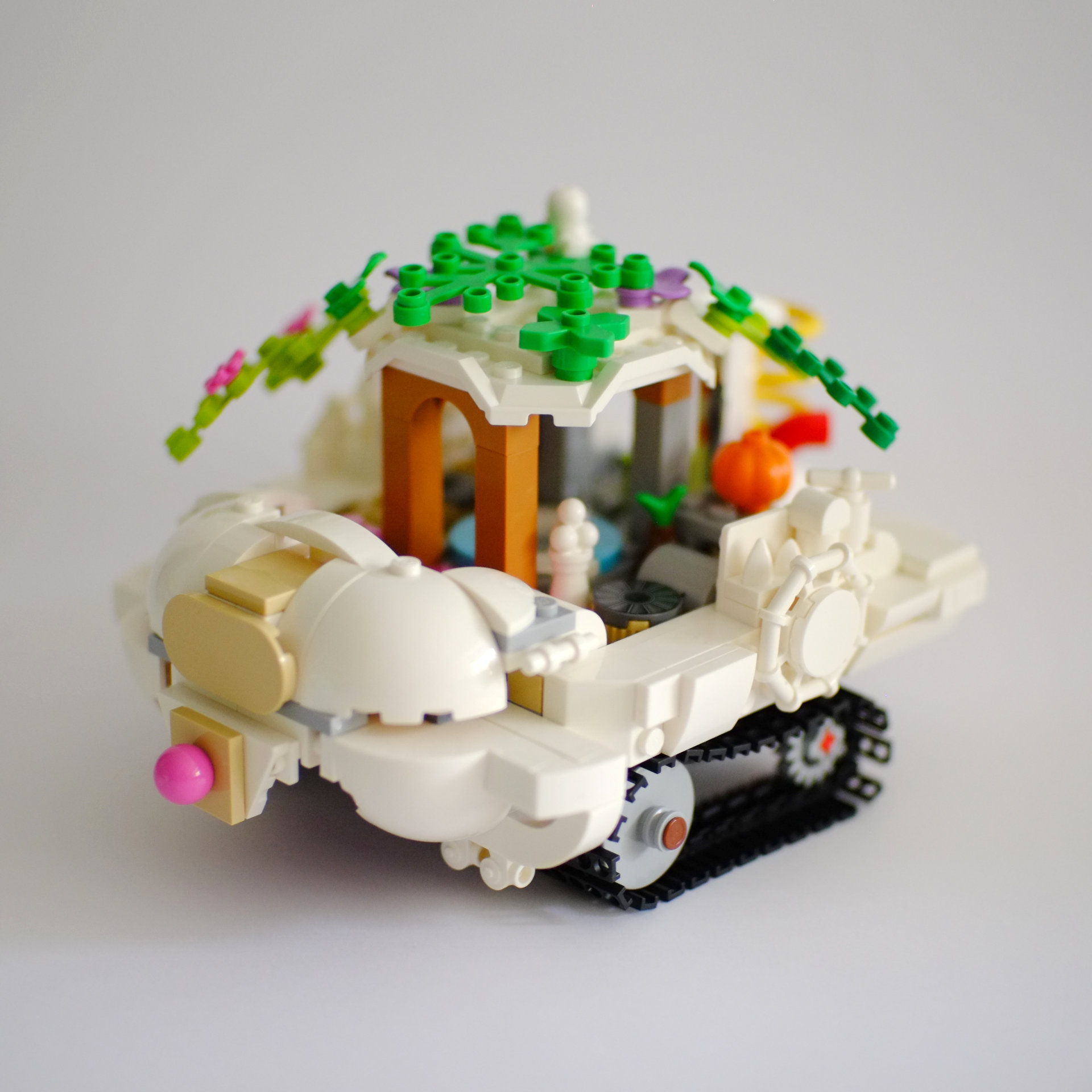 A photo of the left side and the front of a lego build that is a white tourist boat on tank tracks. The roof of the boat is covered with foliage with birds sitting on top.