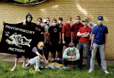 A photo of a group of people in masks posing in front of a yellow brick wall with an Antifascist Action banner